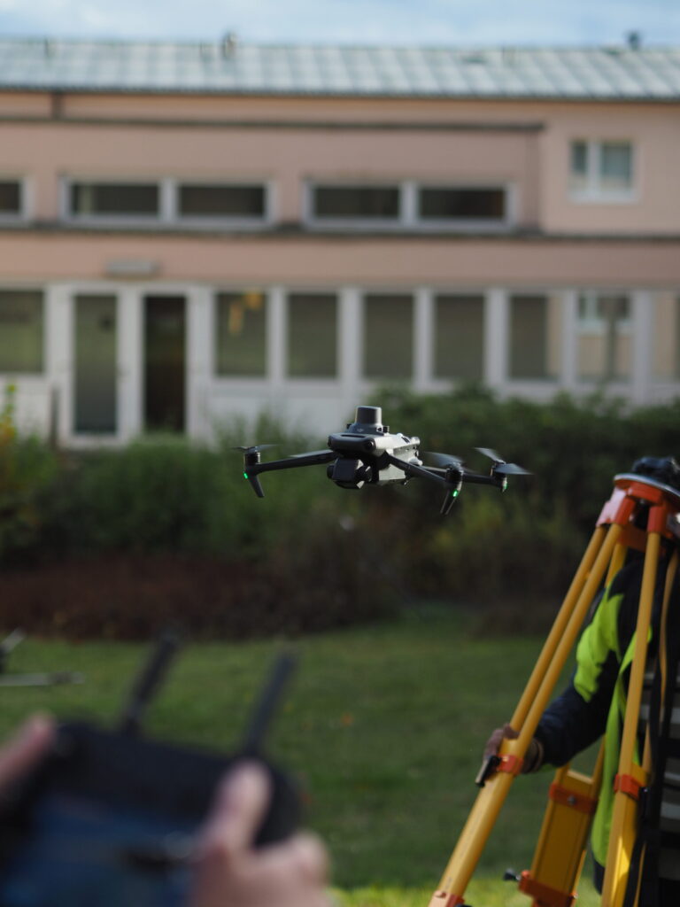 Drohne ueber einem Passpunkt, daneben der GNSS-Empfaenger, mit dem der Punkt eingemessen wurde.